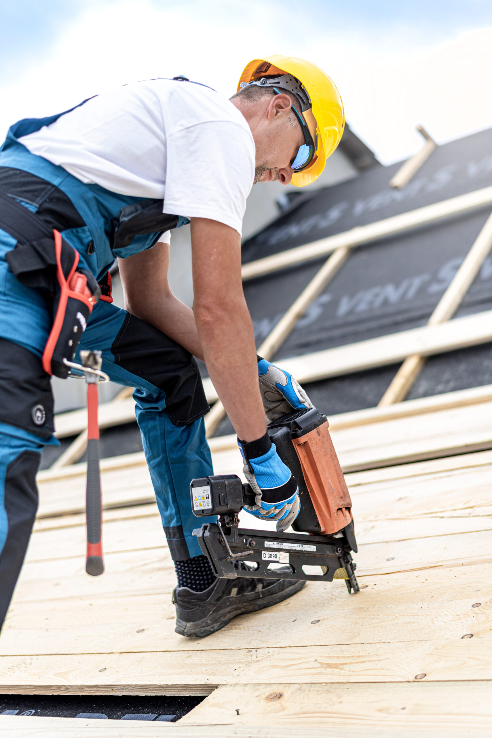 Professional roofer wearing safety gear using a nail gun to secure shingles on a residential roof during installation